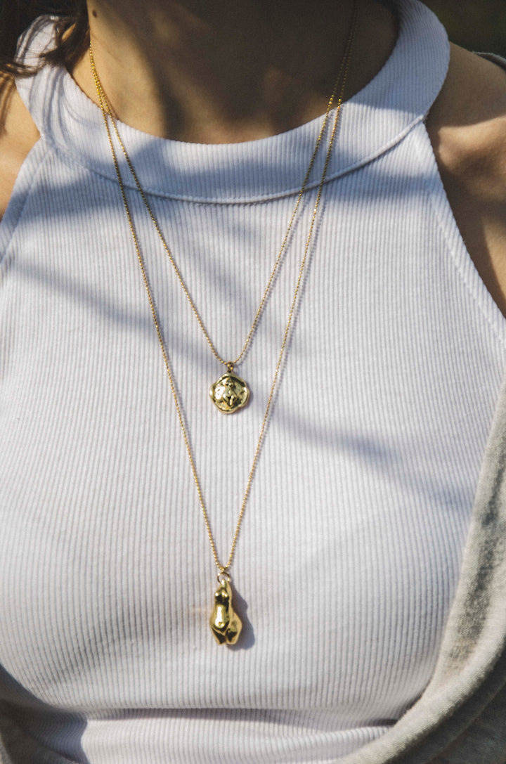 Handcrafted brass Venus coin pendant necklace by Atelier Objectora, with a textured, timeworn aesthetic depicting a female figure on a gold-plated steel chain, evoking the essence of ancient artifacts.
Ručne vyrobený mosadzný náhrdelník s medailonom Venuše od Atelier Objectora, s textúrovaným dizajnom a patinovaným vzhľadom, zobrazujúcim ženskú postavu na pozlátenej oceľovej retiazke, pripomínajúci starodávne artefakty.